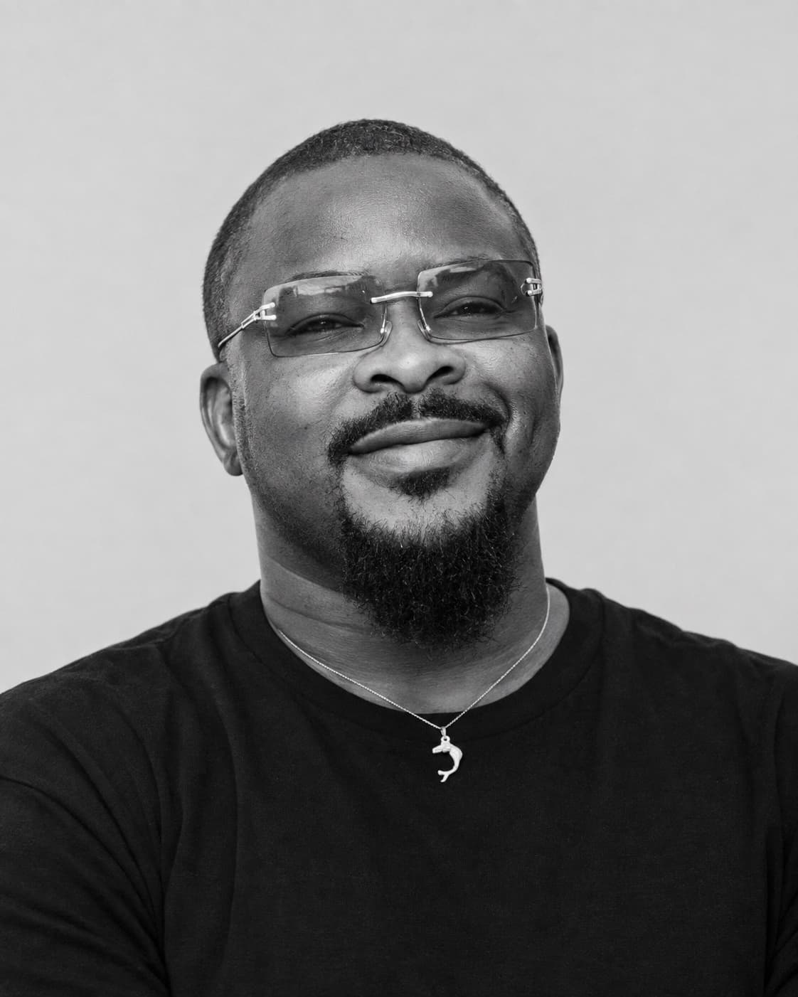 Opeyemi Bangkok, in a black T-shirt and rimless glasses, smiling at the camera